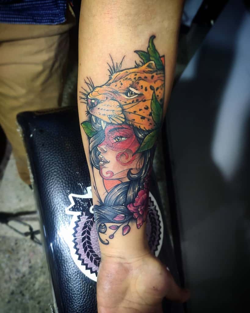 A bold tattoo of a jaguar seemingly biting the head of a woman, with vivid colors, detailed shading, and floral accents on the forearm for a dramatic effect.