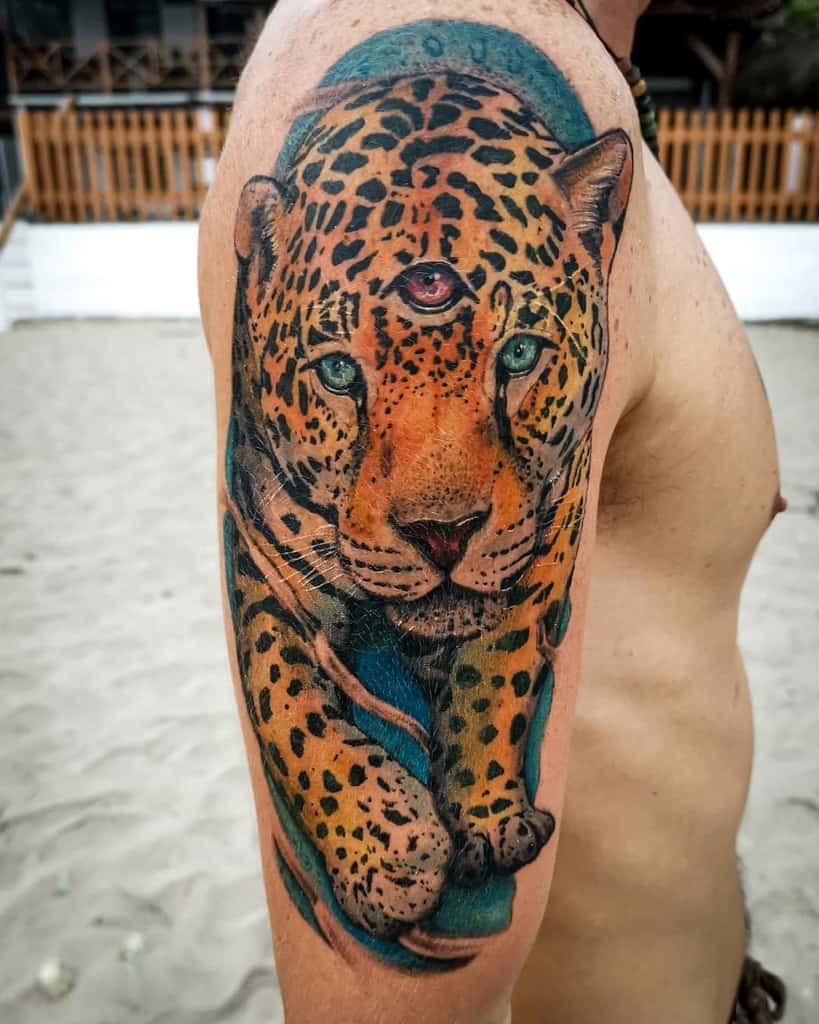 A vibrant and colorful tattoo of a jaguar with a third eye in the center of its forehead, featuring bold shading and intricate details, placed on the upper arm.