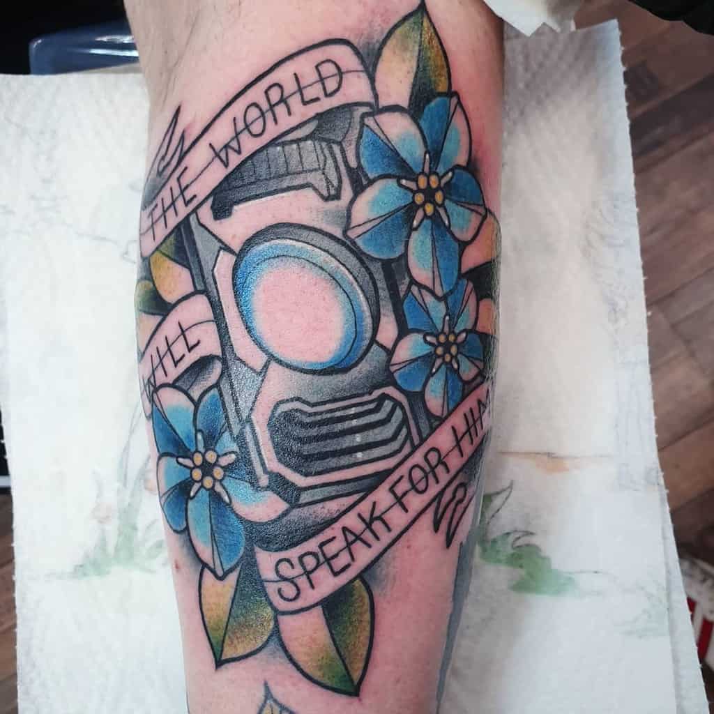 Elegant Halo tattoo featuring Guilty Spark 343, blue flowers, and a banner reading 'The world will speak for him,' inked on the forearm.
