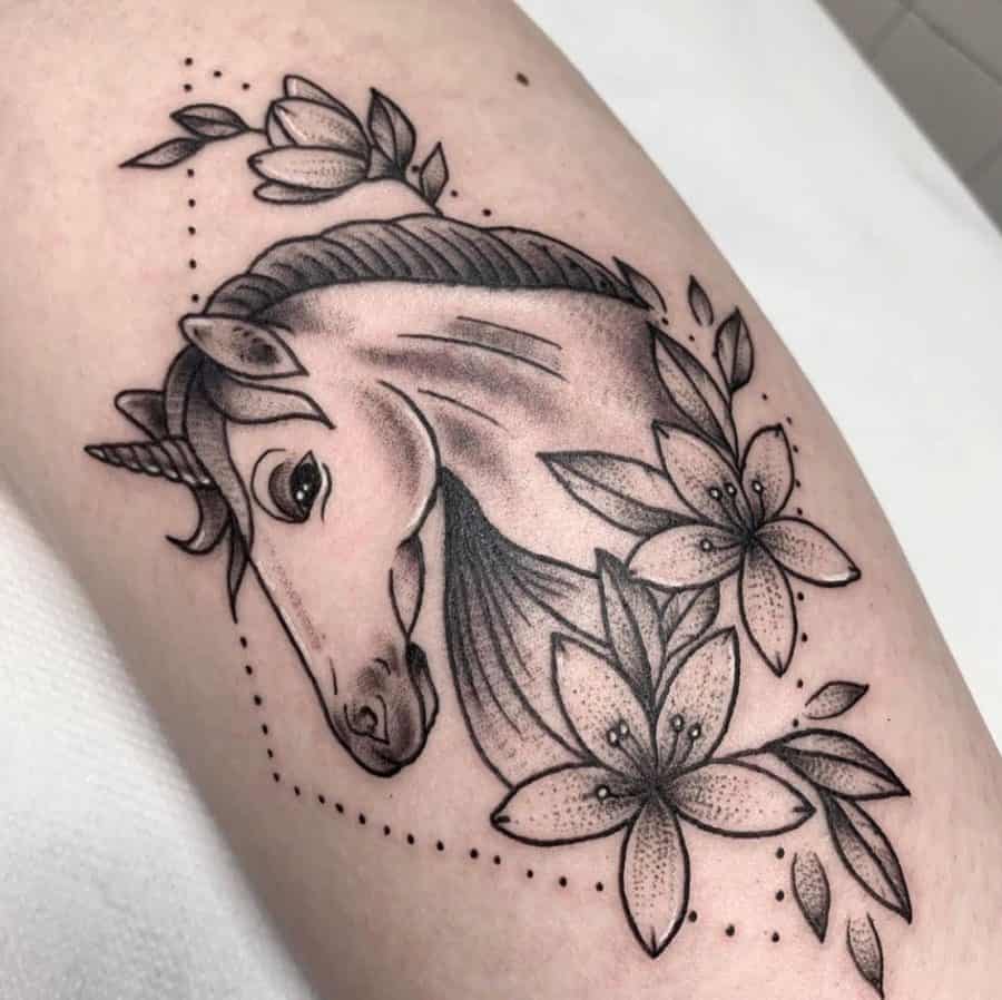 Elegant black ink tattoo of a unicorn’s head, surrounded by blooming flowers and delicate dotted accents for a soft, mystical look.