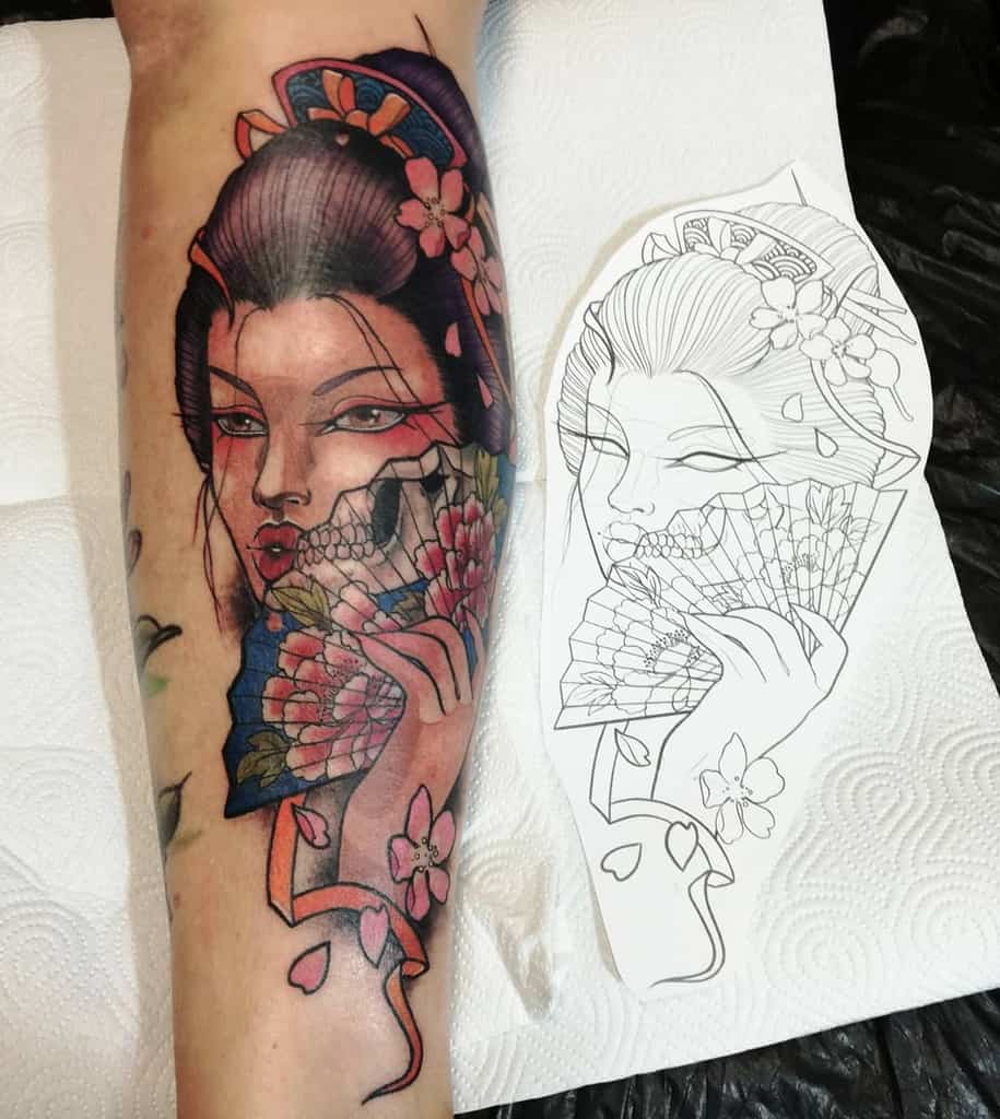 Colorful Geisha tattoo on forearm with a half-skull face, holding a floral fan, blending beauty and mortality in a striking design.