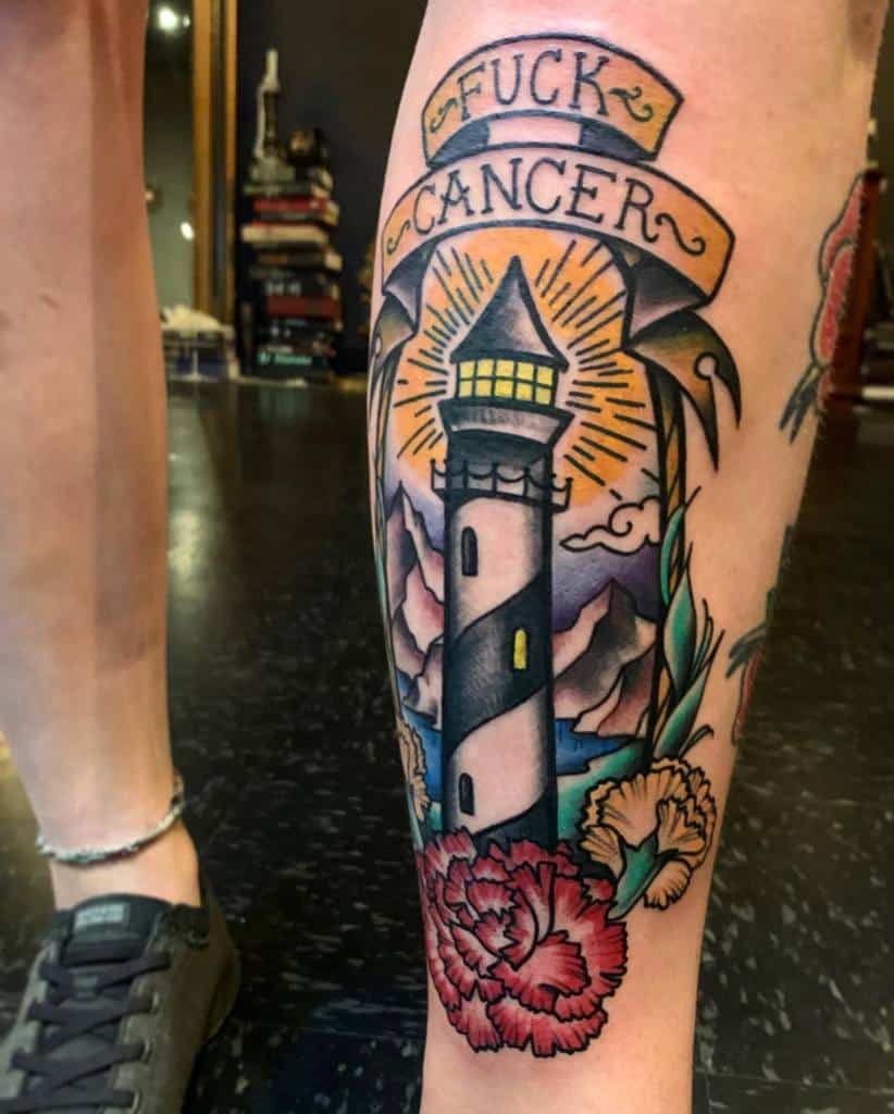 Tattoo featuring a lighthouse, carnation, clouds, mountains, and a ribbon with "F*** Cancer" message