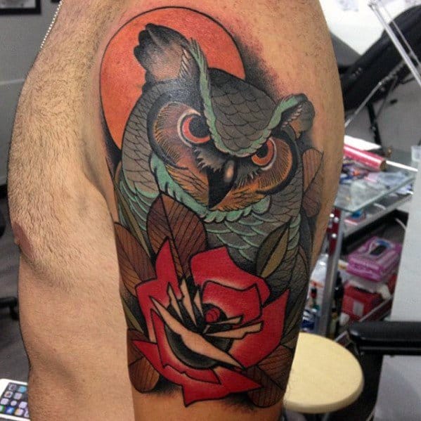 Neo-traditional owl tattoo with piercing orange eyes, a bold red rose, and a glowing sunset backdrop, creating a striking upper arm design.