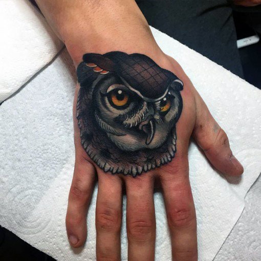 Neo-traditional owl hand tattoo with bold shading, piercing orange eyes, and intricate feather details, creating a striking and detailed design.