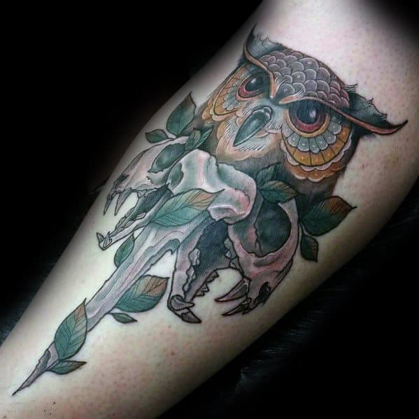 Neo-traditional owl tattoo with intricate feather details, a skull, dagger, and leaf accents, creating a dark and mystical forearm design.