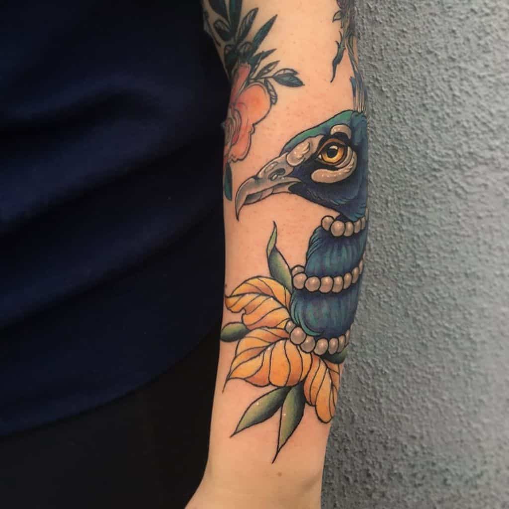 Peacock tattoo with a pearl necklace and vibrant sunflower, located on the forearm.