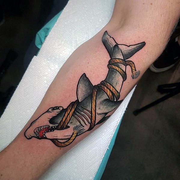 Neo-traditional shark tattoo on the arm with orange rope tightly wrapped around its body, showing teeth and visible wounds.