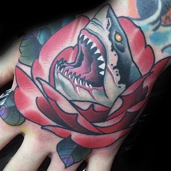 Neo-traditional hand tattoo of a roaring shark emerging from a vivid red rose with bold outlines and piercing orange eye.