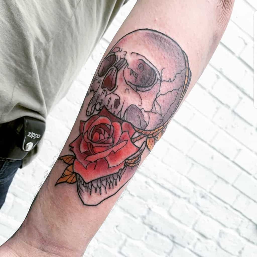 Forearm tattoo of a cracked skull with a vibrant red rose, featuring bold linework and subtle shading for a striking contrast.