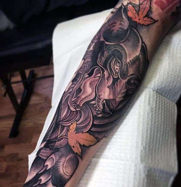 Arm tattoo of a stylized Japanese wolf intricately woven with swirling patterns and autumn leaves