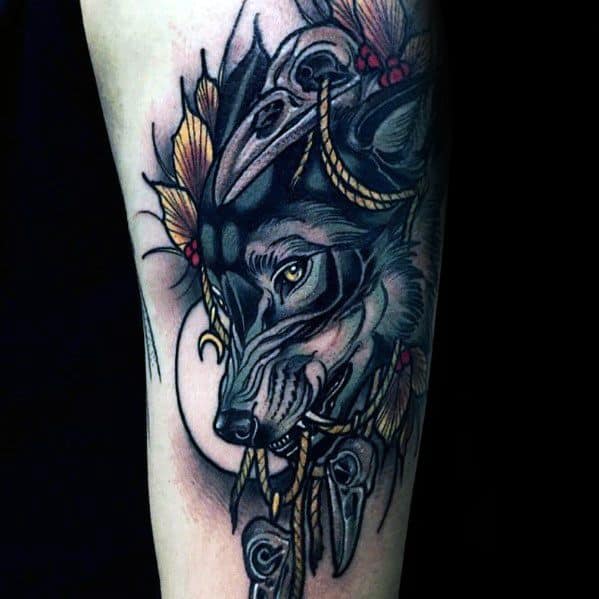 Neo-traditional tattoo of a mystical wolf with golden eyes, adorned with skulls, feathers, and ropes, featuring intricate shading and bold details.