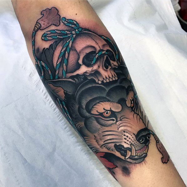 Neo-traditional tattoo of a snarling wolf with piercing eyes, a skull tied with blue rope, bold shading, and intricate detailing for a fierce look.
