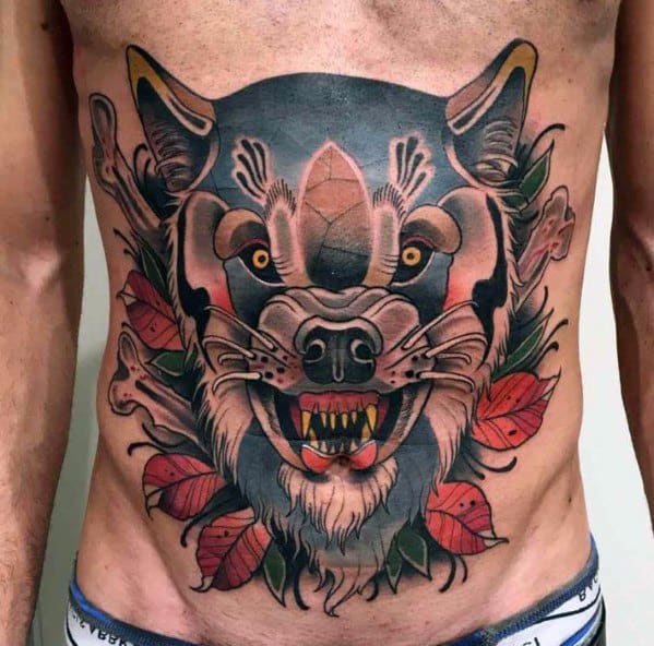 Neo-traditional stomach tattoo of a snarling wolf with piercing eyes, tribal markings, autumn leaves, and crossed bones for a fierce, bold design.