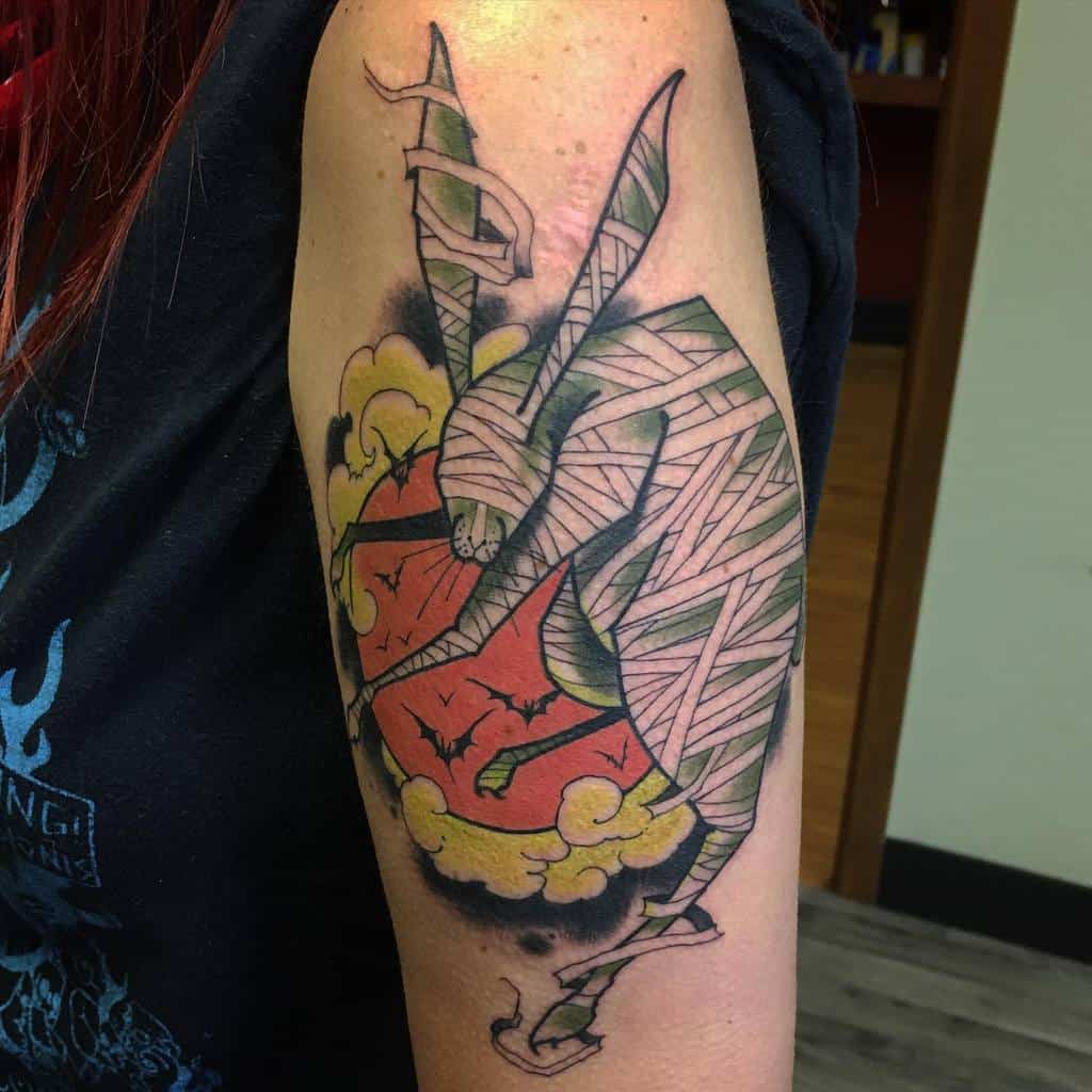 Bold tattoo of a rabbit wrapped in bandages hugging a red moon with flying bats, surrounded by yellow clouds