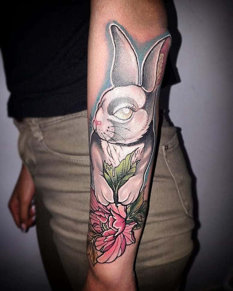 Detailed tattoo of a rabbit with soft shading holding a leaf with vibrant pink flowers