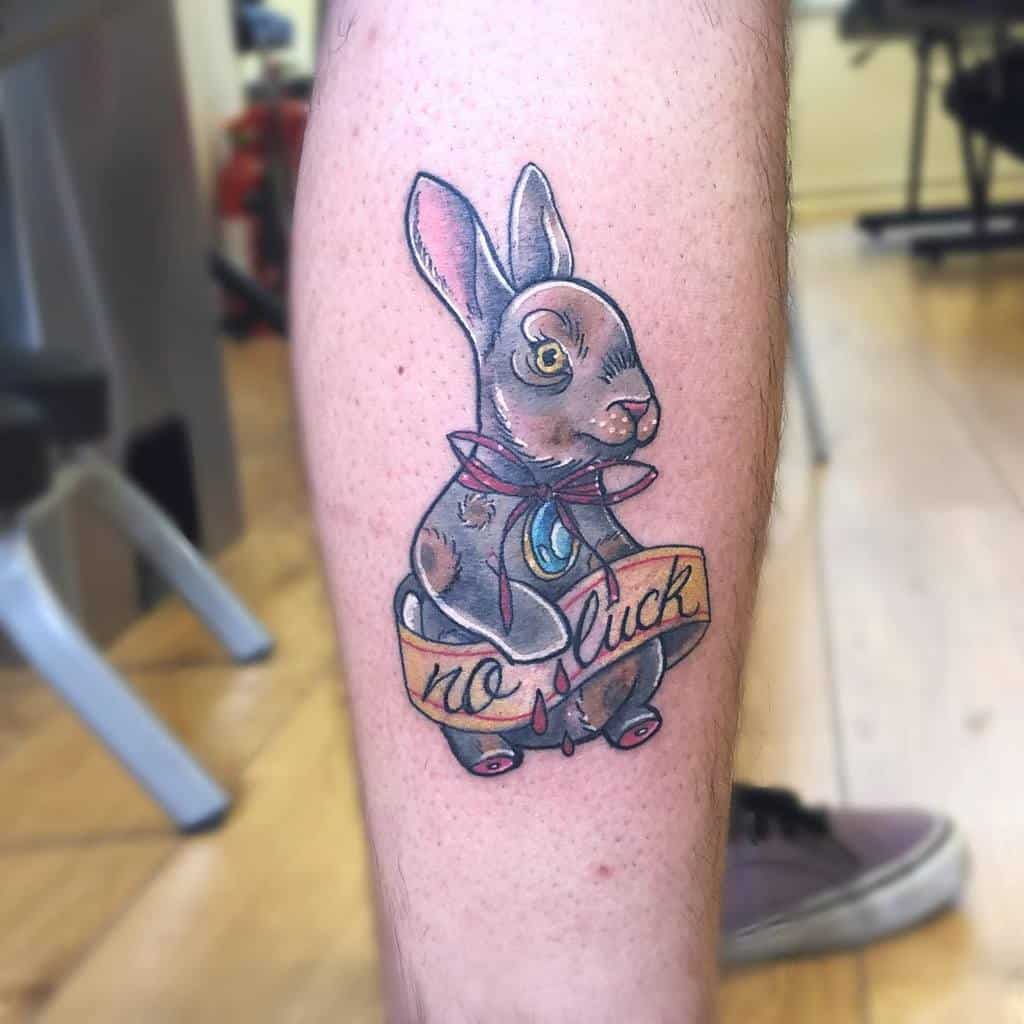 Whimsical tattoo of a rabbit wearing a bow tie, with a 'no luck' banner beneath it, featuring vibrant colors and bold shading