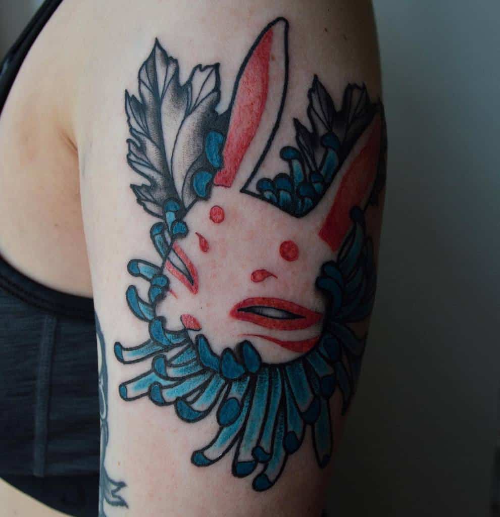 Bold tattoo of a rabbit with stylized red markings, surrounded by intricate blue flowers and leaves
