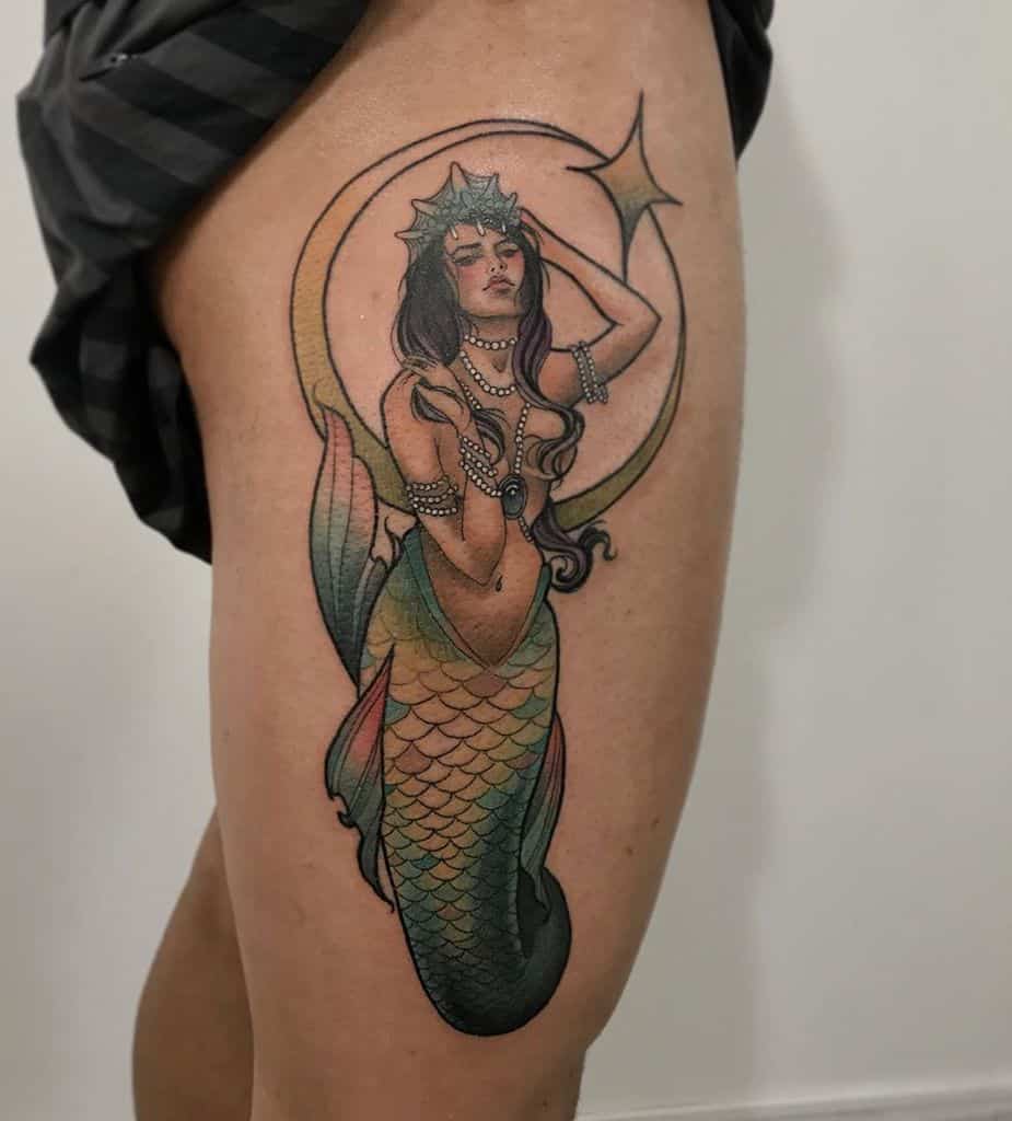 Tattoo of a siren with flowing hair and jeweled accessories, framed by a crescent moon and star on a leg
