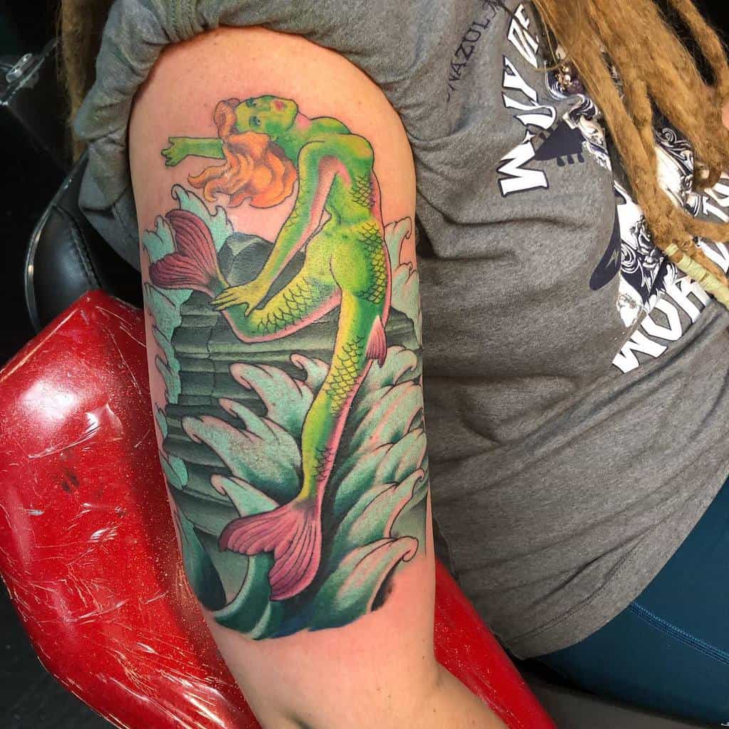 Vibrant neo-traditional arm tattoo of a green mermaid with orange hair, surrounded by ocean waves and bold details