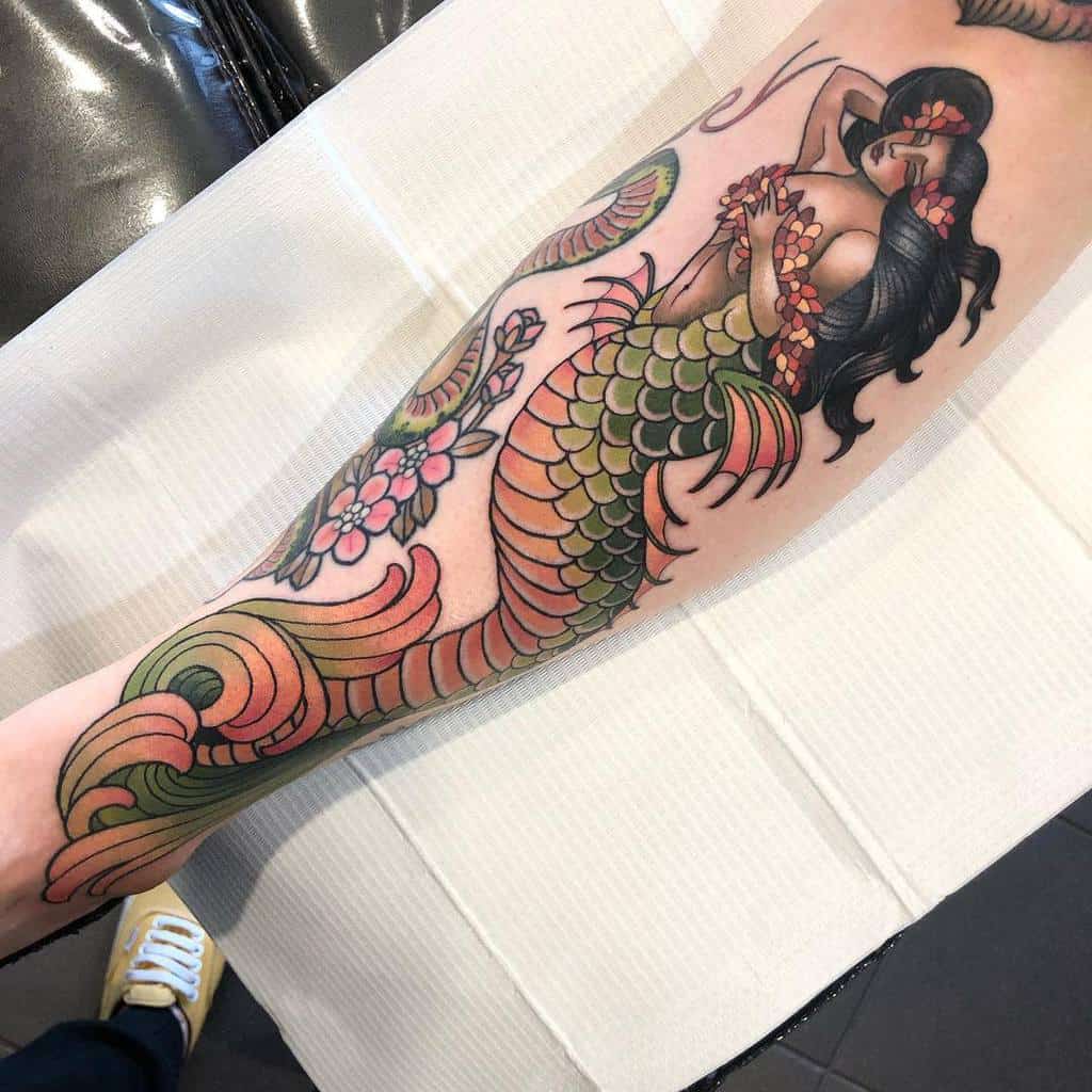Vibrant neo-traditional tattoo of a mermaid with colorful scales, floral accents, and flowing black hair on the forearm