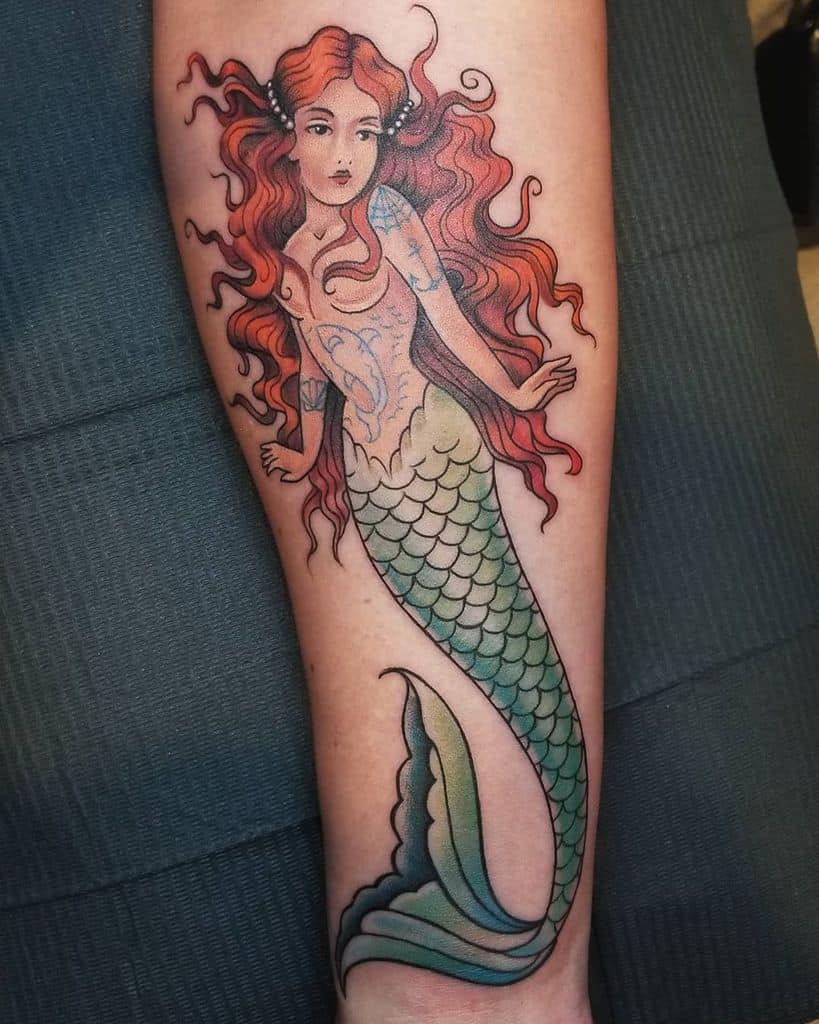 Neo-traditional tattoo of a vibrant mermaid with flowing red hair, pearly accents, and shimmering green scales on the forearm