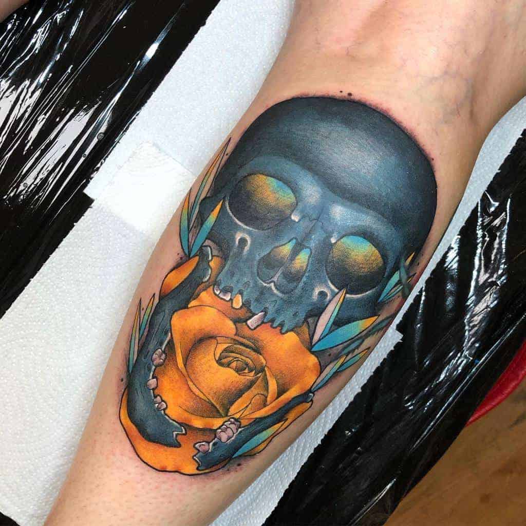 Tattoo of a blue skull with a yellow rose on a person's thigh