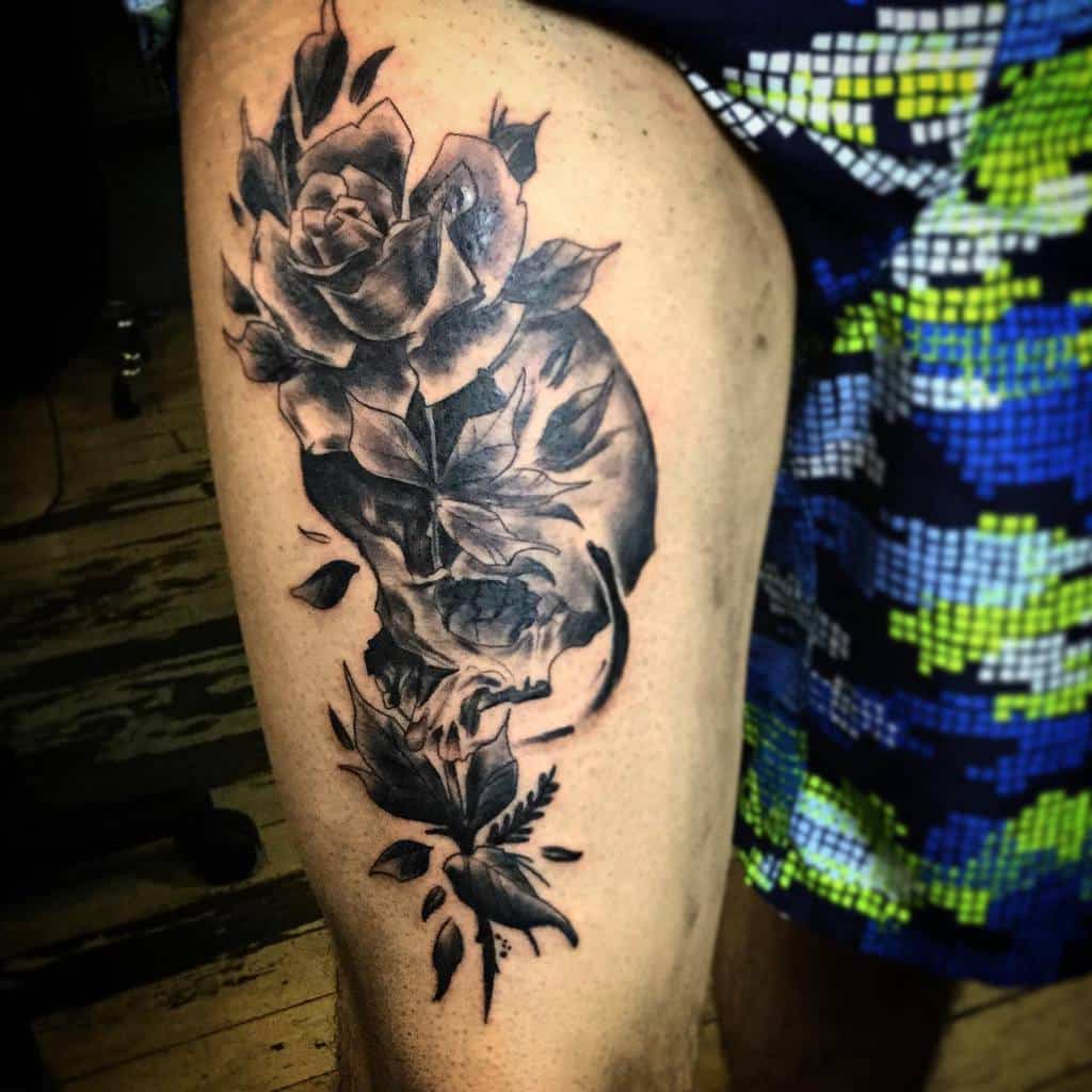 Black and grey thigh tattoo of a skull seamlessly blending into roses and leaves, creating a surreal and artistic design.