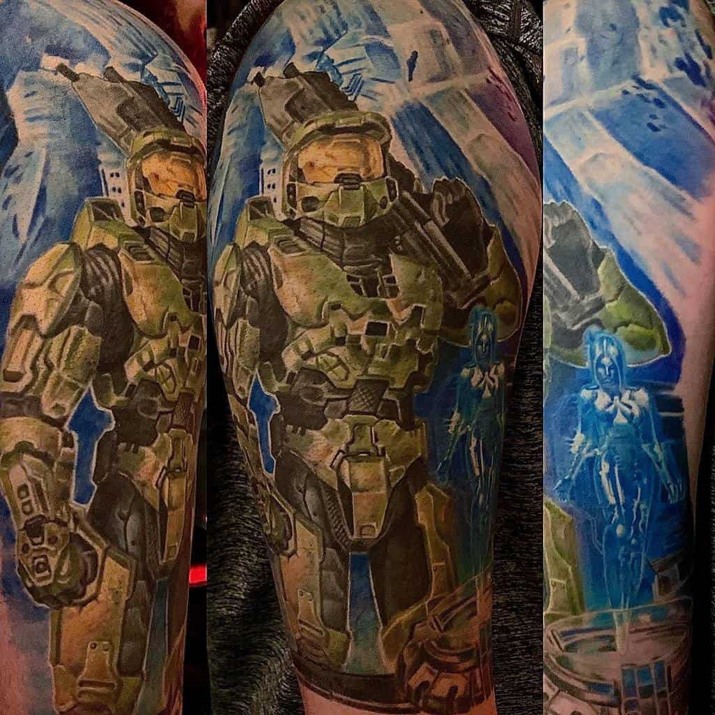 Full-arm Halo tattoo featuring Master Chief in green Mjolnir armor with Cortana’s hologram, set against a blue sci-fi backdrop.