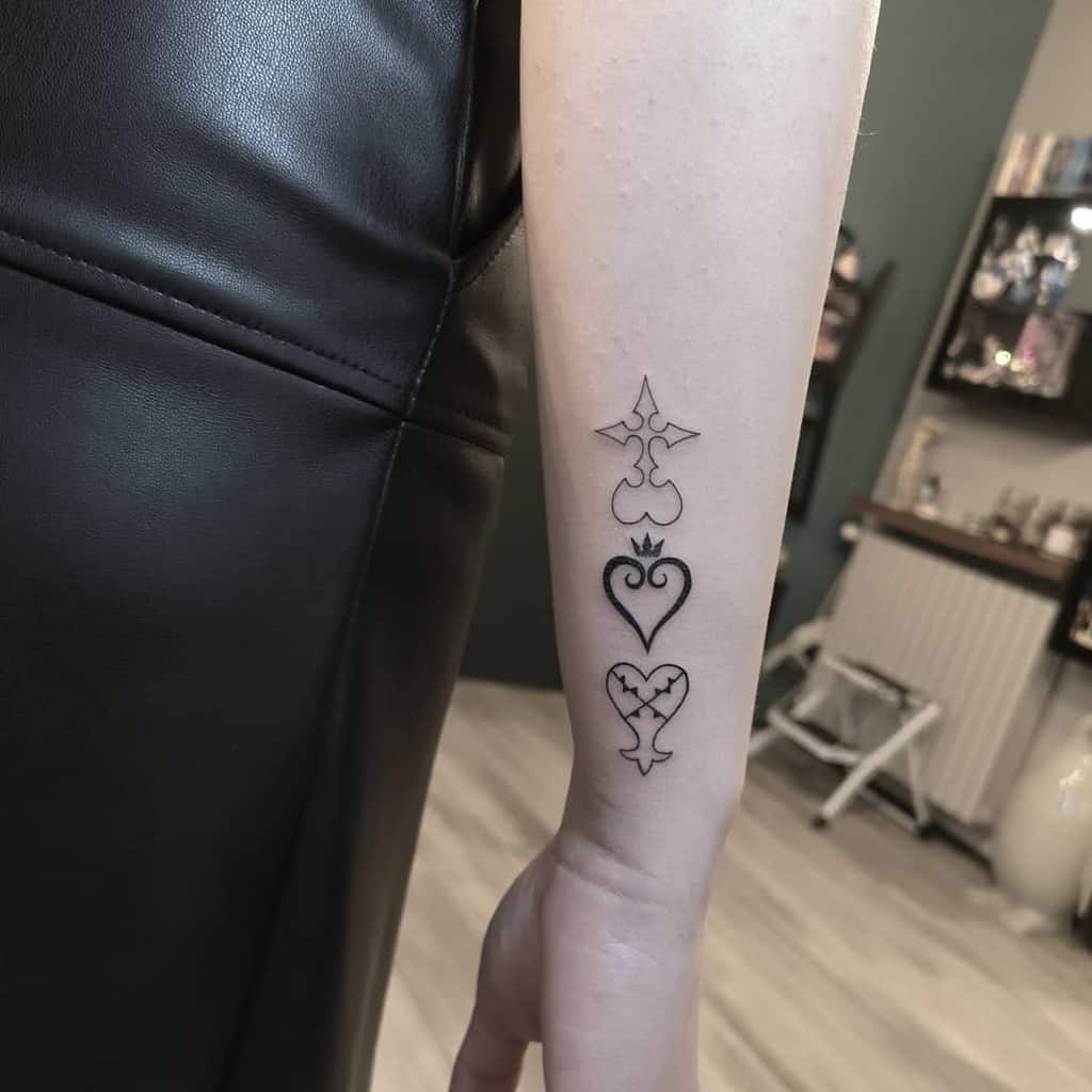 Minimalist black ink tattoo of Kingdom Hearts faction symbols—Nobodies, Heartless, and Unversed—vertically aligned on the forearm.