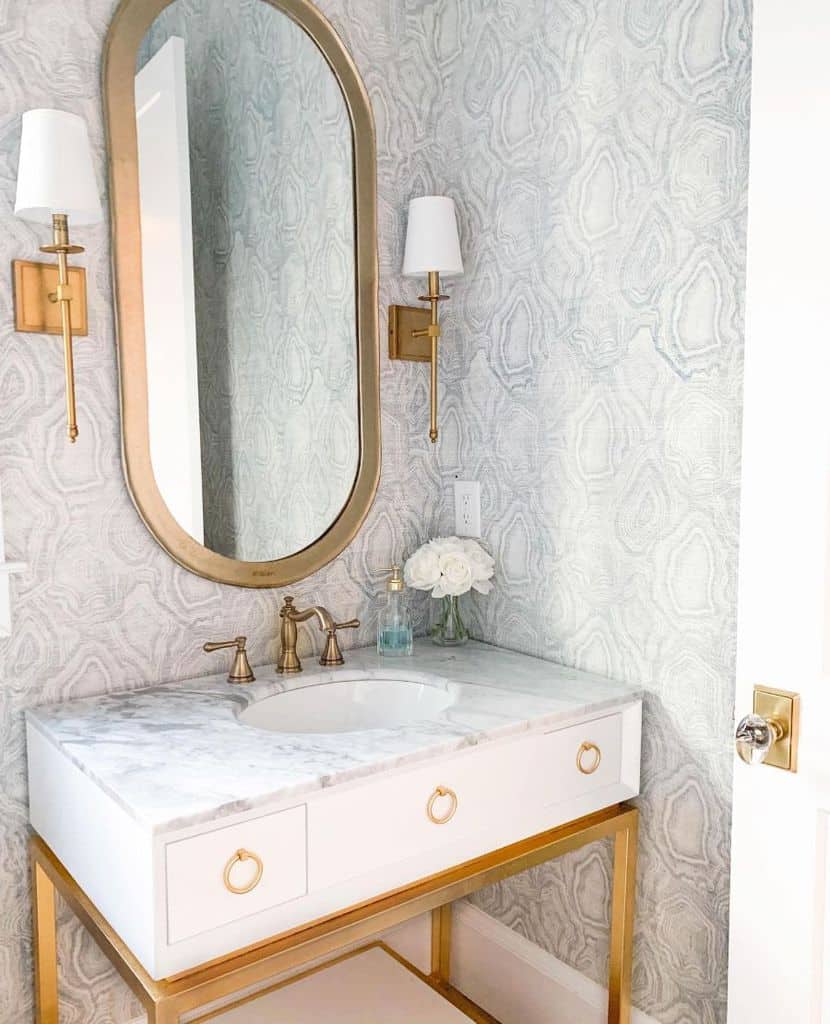 Bathroom with textured wallpaper, marble vanity, gold mirror, and wall sconces.