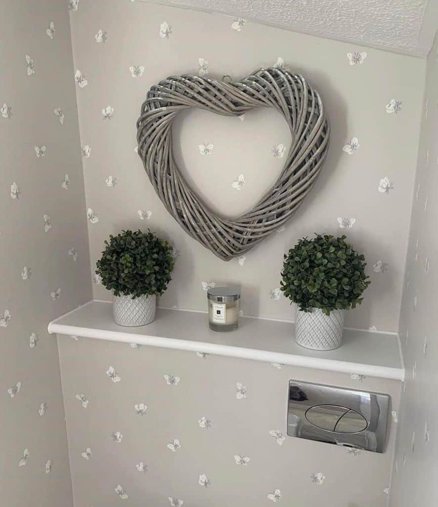 Gray bathroom with butterfly wallpaper, wicker heart wall art, and decorative plants on shelf.