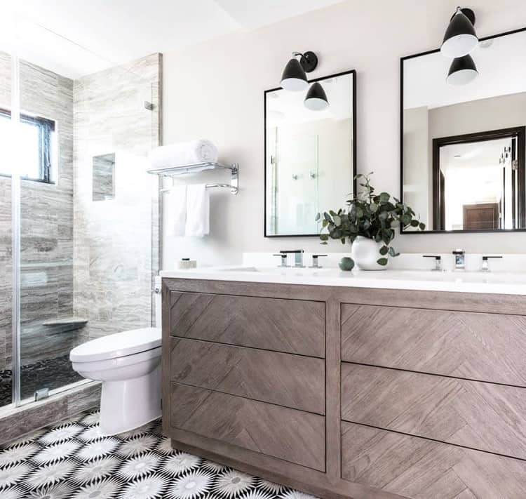 Modern farmhouse bathroom with a wooden double vanity, mirrored cabinets, glass shower, and patterned floor tiles