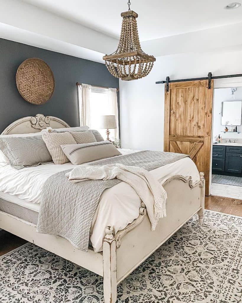 Cozy farmhouse bedroom with a vintage bed, gray accent wall, barn door, and a woven chandelier