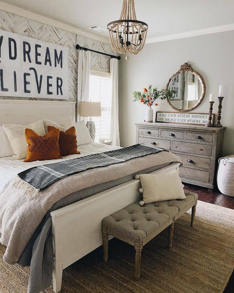 Cozy farmhouse bedroom with rustic style, featuring a bed, wooden dresser, decorative pillows, and a round mirror