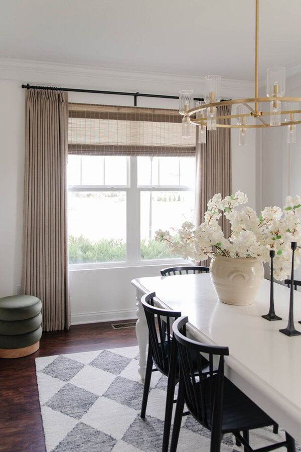 Modern dining room with neutral greige curtains, a gold chandelier, and a white table with black chairs.
