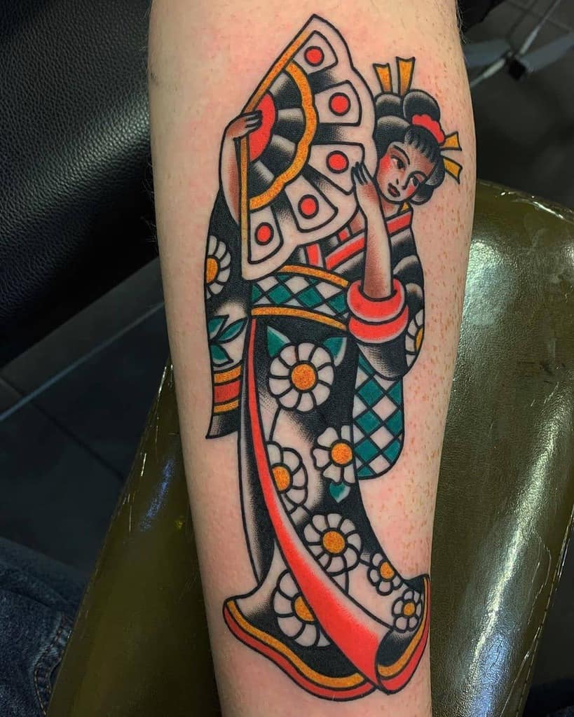 Traditional-style Geisha tattoo on the forearm, featuring bold black outlines, vibrant red, yellow, and green colors, and floral kimono details.