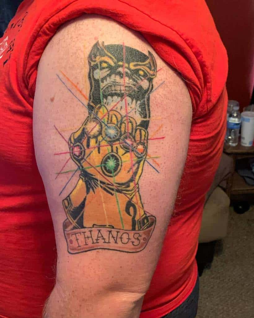 Vibrant Thanos tattoo featuring the Infinity Gauntlet, bursting with energy lines and bold colors, with a banner reading 'Thanos'