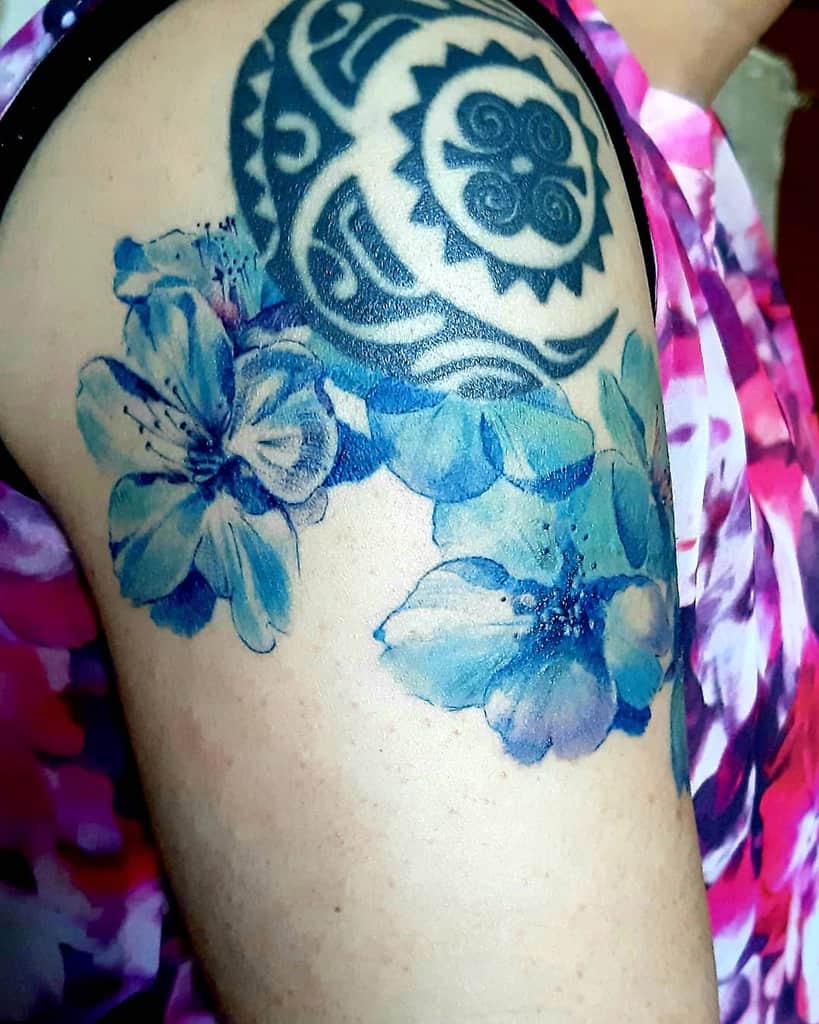 Vibrant tattoo featuring a bold tribal design in black ink, complemented by watercolor-style blue flowers for a striking contrast