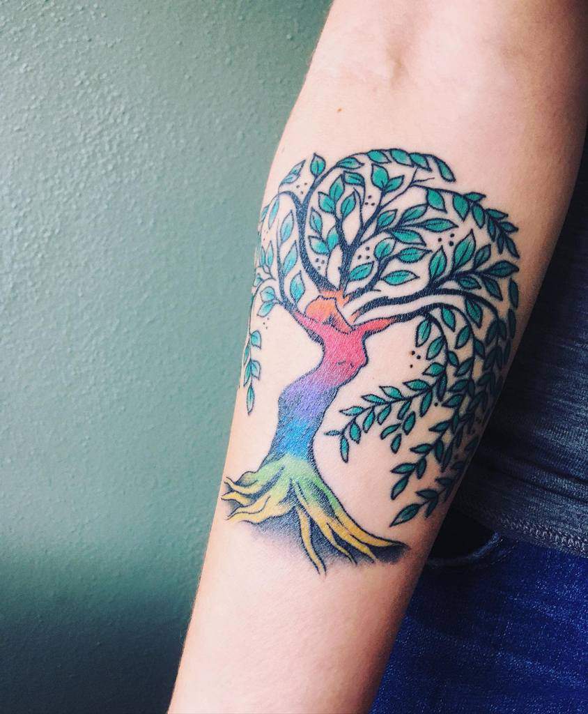 Vibrant tree of life woman tattoo with a rainbow-colored trunk, lush green leaves, and deep roots, symbolizing growth and diversity