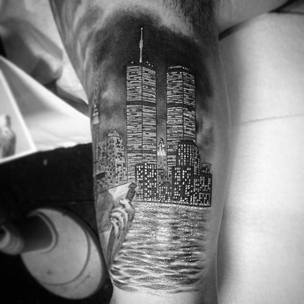 Black and gray tattoo of the Twin Towers reflecting on water, with the Statue of Liberty in the foreground and NYC skyline at night.