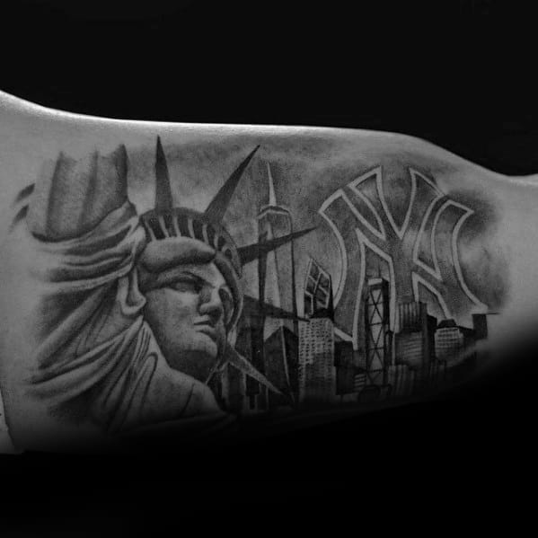Black and gray tattoo of the Statue of Liberty, NYC skyline, and large New York Yankees logo across the upper arm.