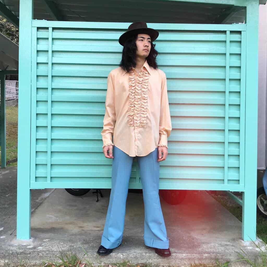 nice top and blue pants with black hat on long hair man