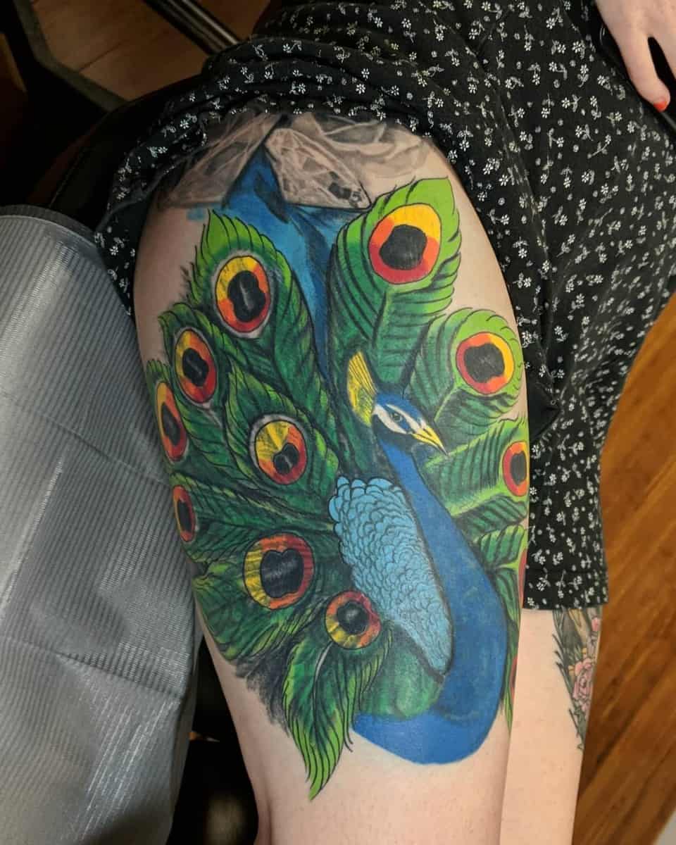 Colorful peacock tattoo on a thigh with detailed feathers and patterns