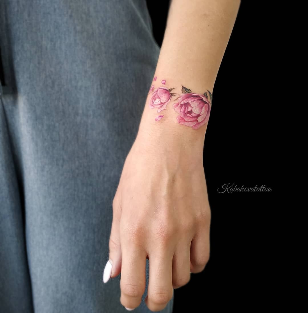 A wrist tattoo of pink roses with greenery on a left arm near the hand