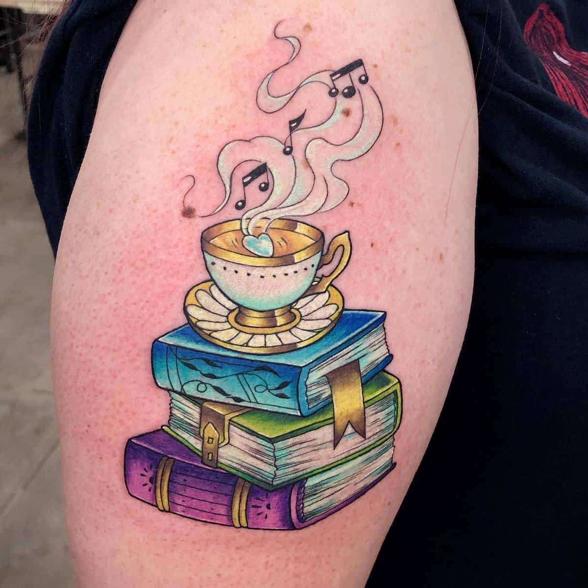 Tattoo of a teacup with musical notes atop a stack of colorful books on an arm