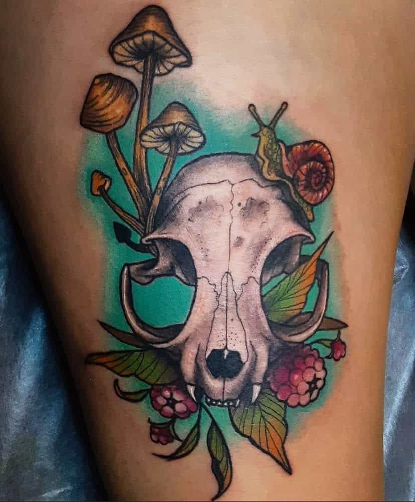 Tattoo of an animal skull with mushrooms, leaves, berries, and a snail