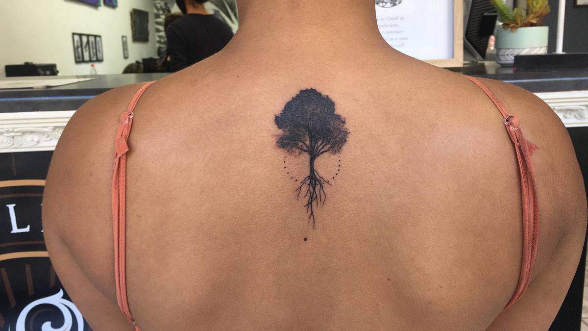 A tattoo of a tree with roots on the upper back, near the shoulder blades