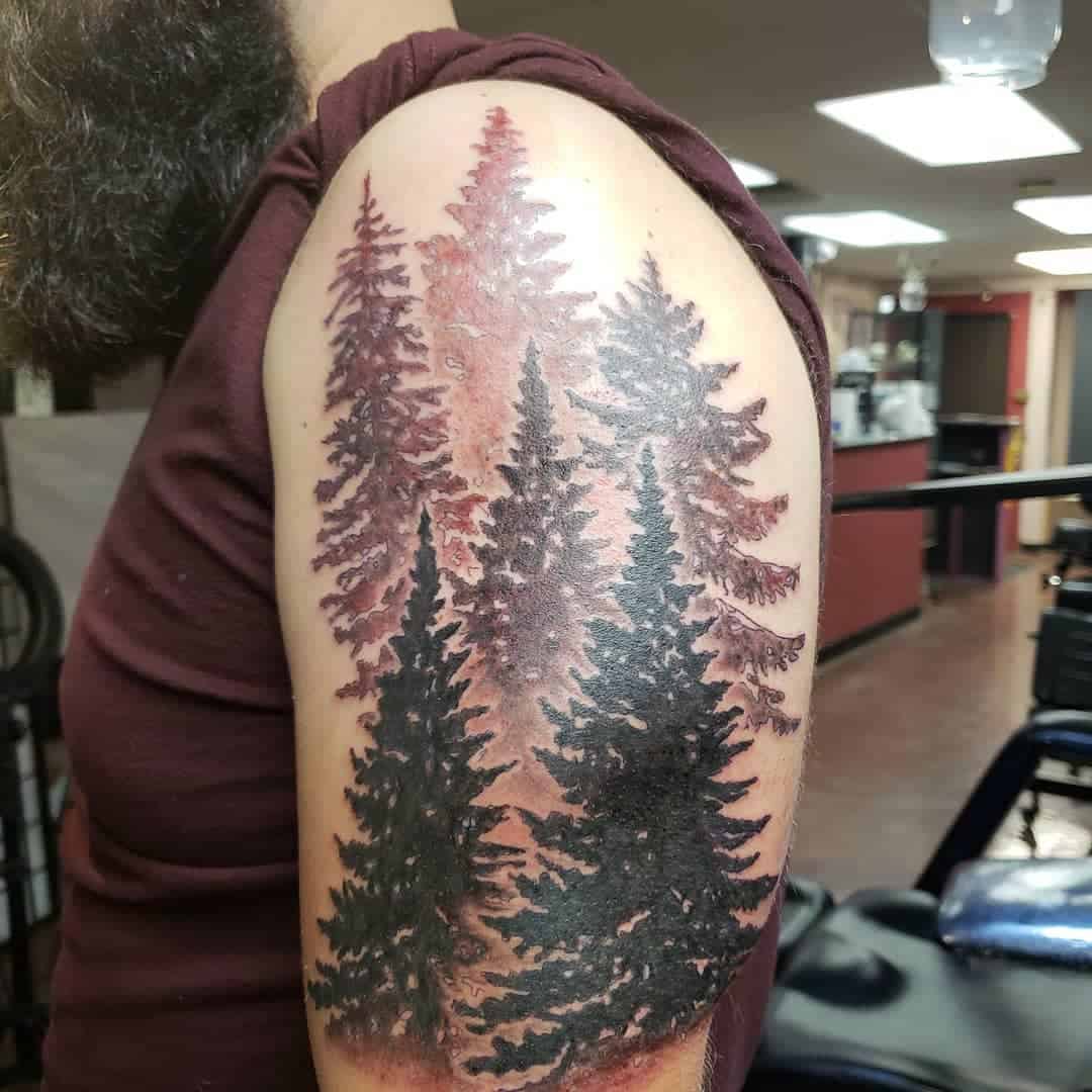 Upper arm tattoo of tall evergreen trees in black and reddish-brown tones