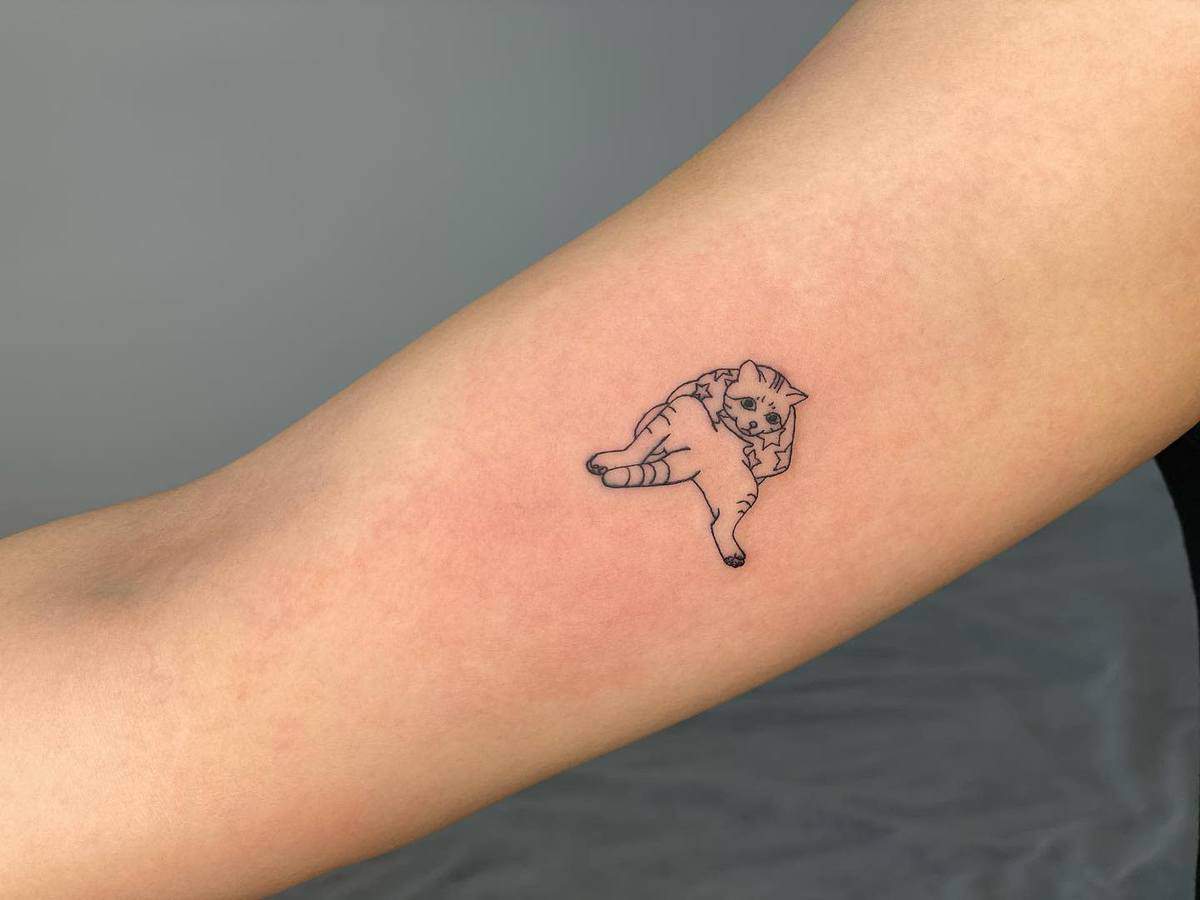 Simple outline tattoo of a lounging cat on an inner arm