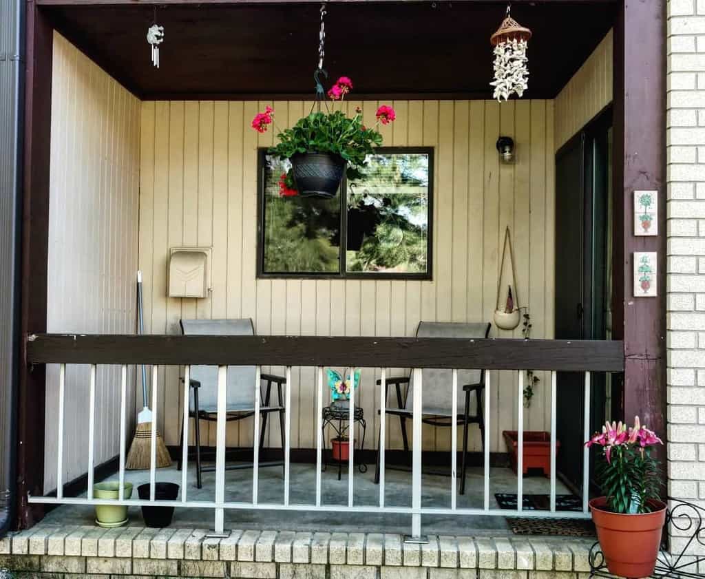 Simple patio with hanging flowers, chairs, potted plants, and cozy seating area under a covered roof.